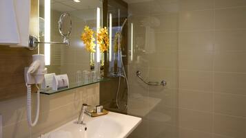 A modern bathroom with a glass shelf holding toiletries, a white sink, a hairdryer, and a mirror with a ring light.