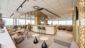 Uma área de estar moderna com sofás, mesas e um bar com banquetas.
