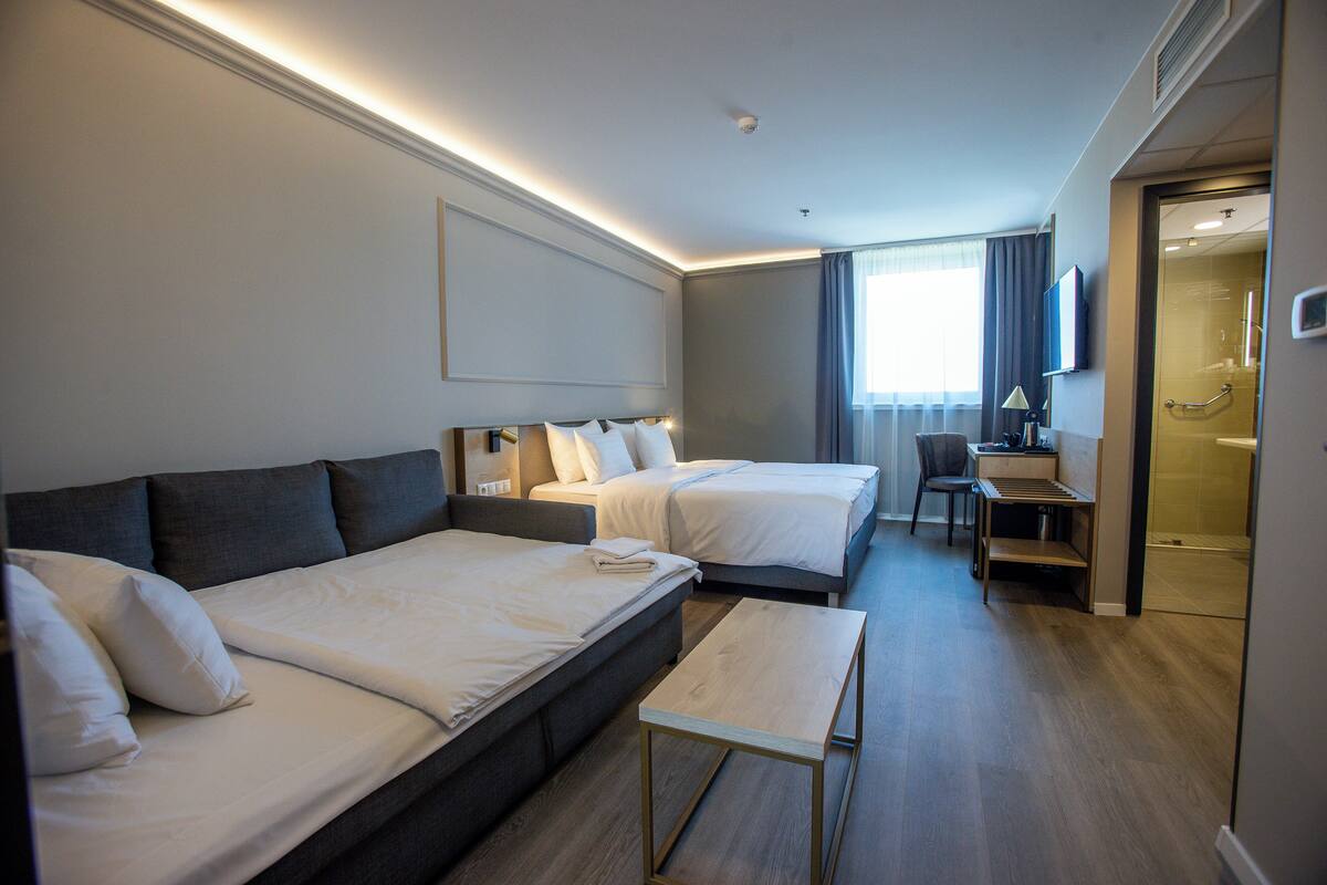 A hotel room with two beds, a desk, and a shower area.