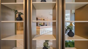 Uma área de recepção com design moderno, com balcão de atendimento, parede decorativa e prateleiras com vasos e plantas.