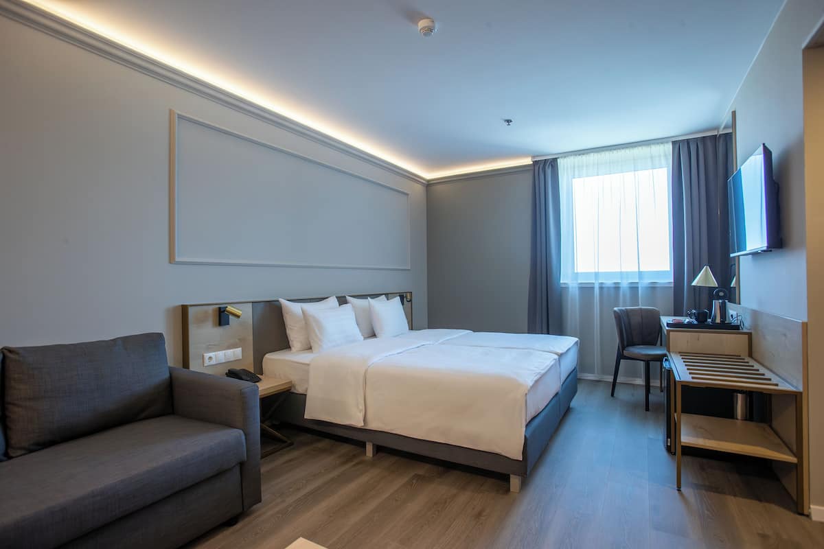 A modern hotel room with a large bed, a sofa, a desk, and a TV.