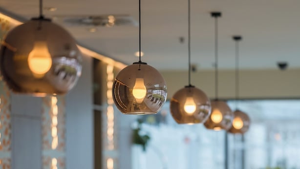 Uma área de recepção moderna com iluminação pendente, plantas em vasos e bancada espelhada.