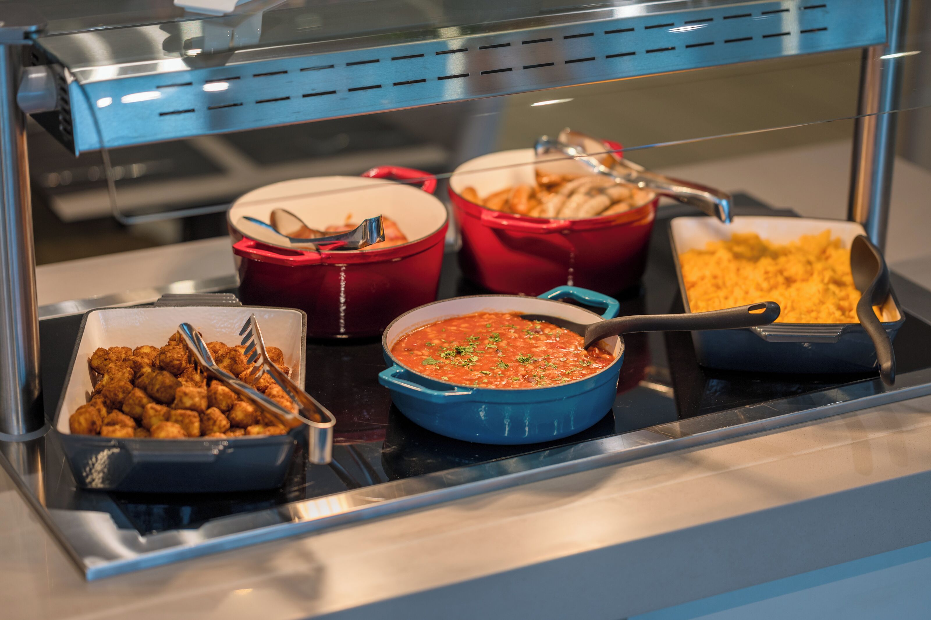 Un buffet con diversi piatti, tra cui crocchette di patate, salsa di pomodoro e una lasagna.