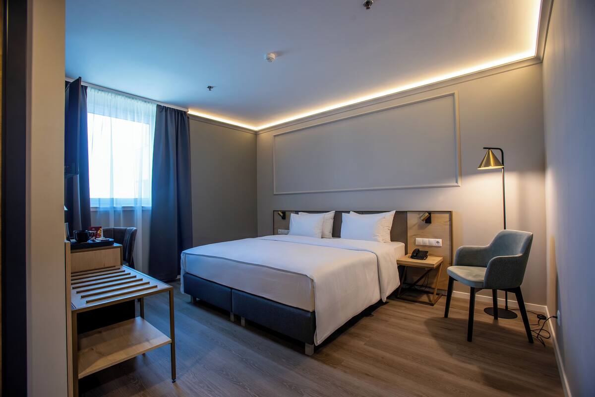 A modern hotel room with a large bed, bedside tables, a desk, and a chair.