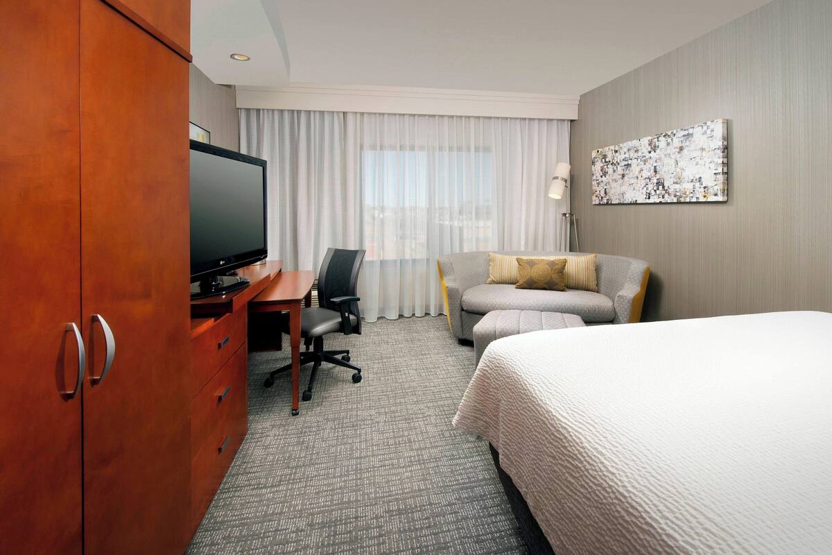 A hotel room with a bed, a desk with a television, a sofa, and a large artwork on the wall.