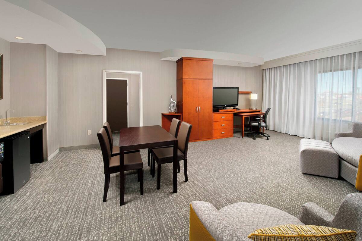 A hotel room with a dining table, chairs, a TV, a desk, and a sofa.