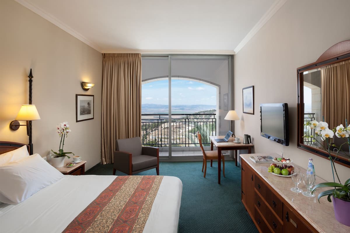 A hotel room with a bed, desk, chair, and a balcony with a view.