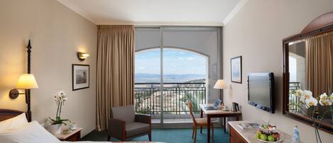 Habitación de hotel con cama, escritorio, silla y balcón con vistas.