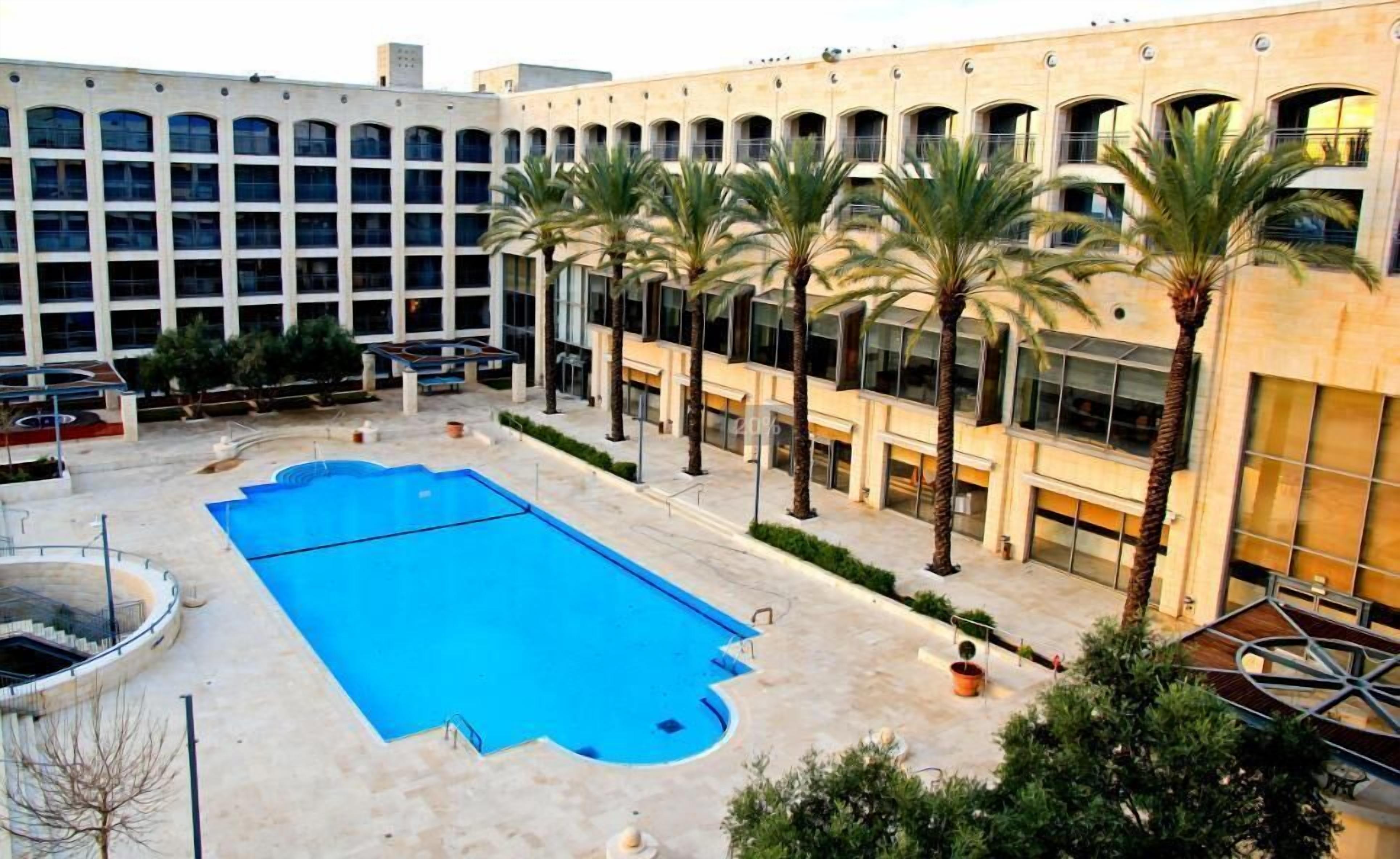 A pool area with a rectangular pool, palm trees, and a building with multiple windows and balconies.