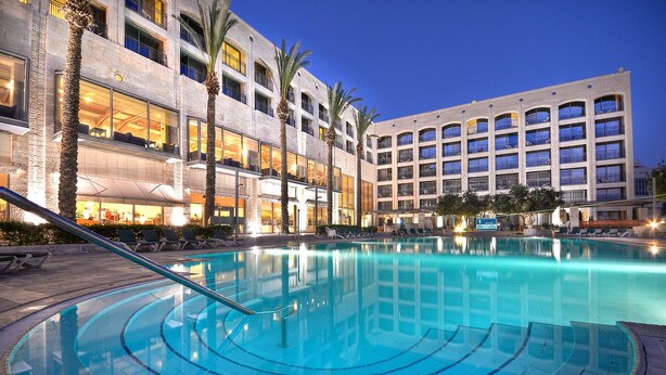 A hotel with a large outdoor pool, palm trees, and a modern building facade. - Golden Crown Hotel (Nazareth)