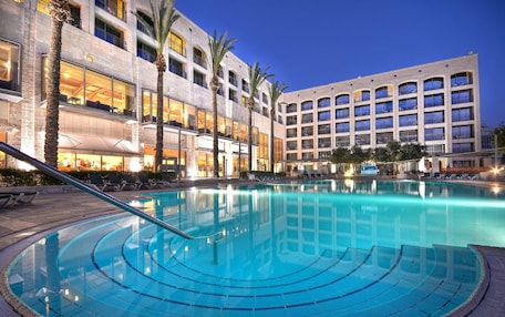 A hotel with a large outdoor pool, palm trees, and a modern building facade.