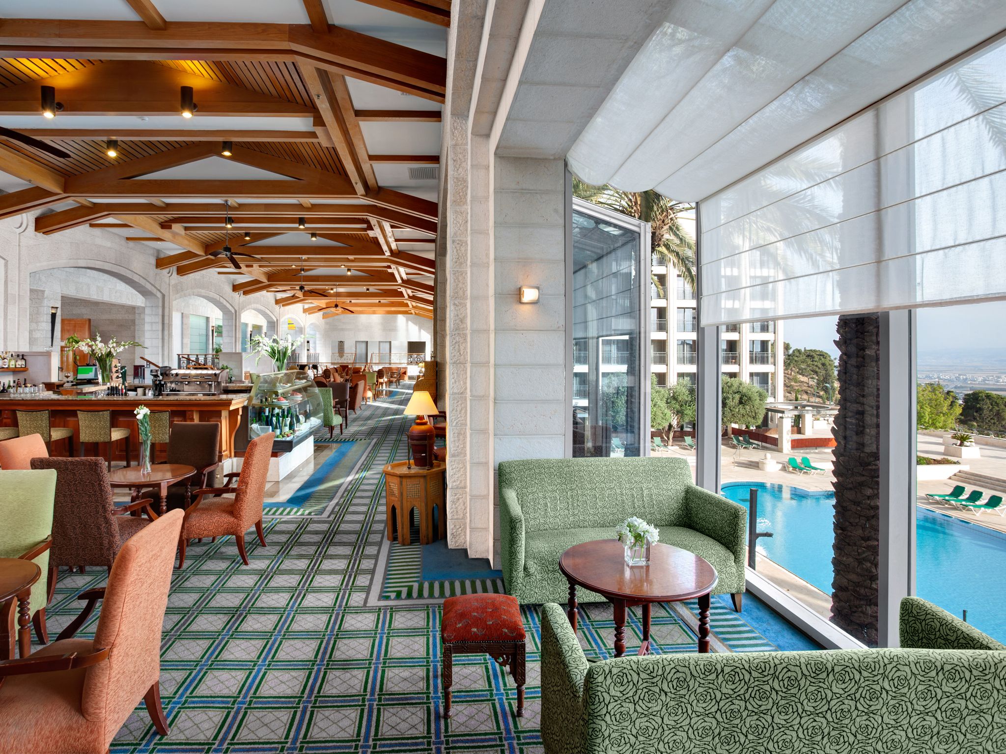 Un amplio espacio interior con piscina, mobiliario verde estampado y una zona de bar.