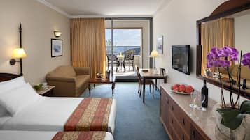 Une chambre d’hôtel avec deux lits, un bureau, une chaise, une table à manger et un balcon avec vue.
