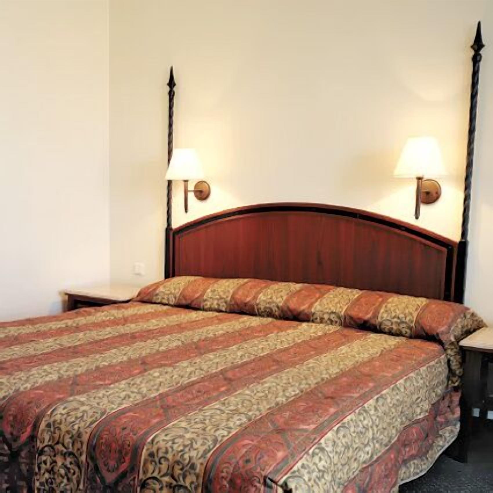 A hotel room with a wooden bed, two bedside lamps, and a patterned bedspread.