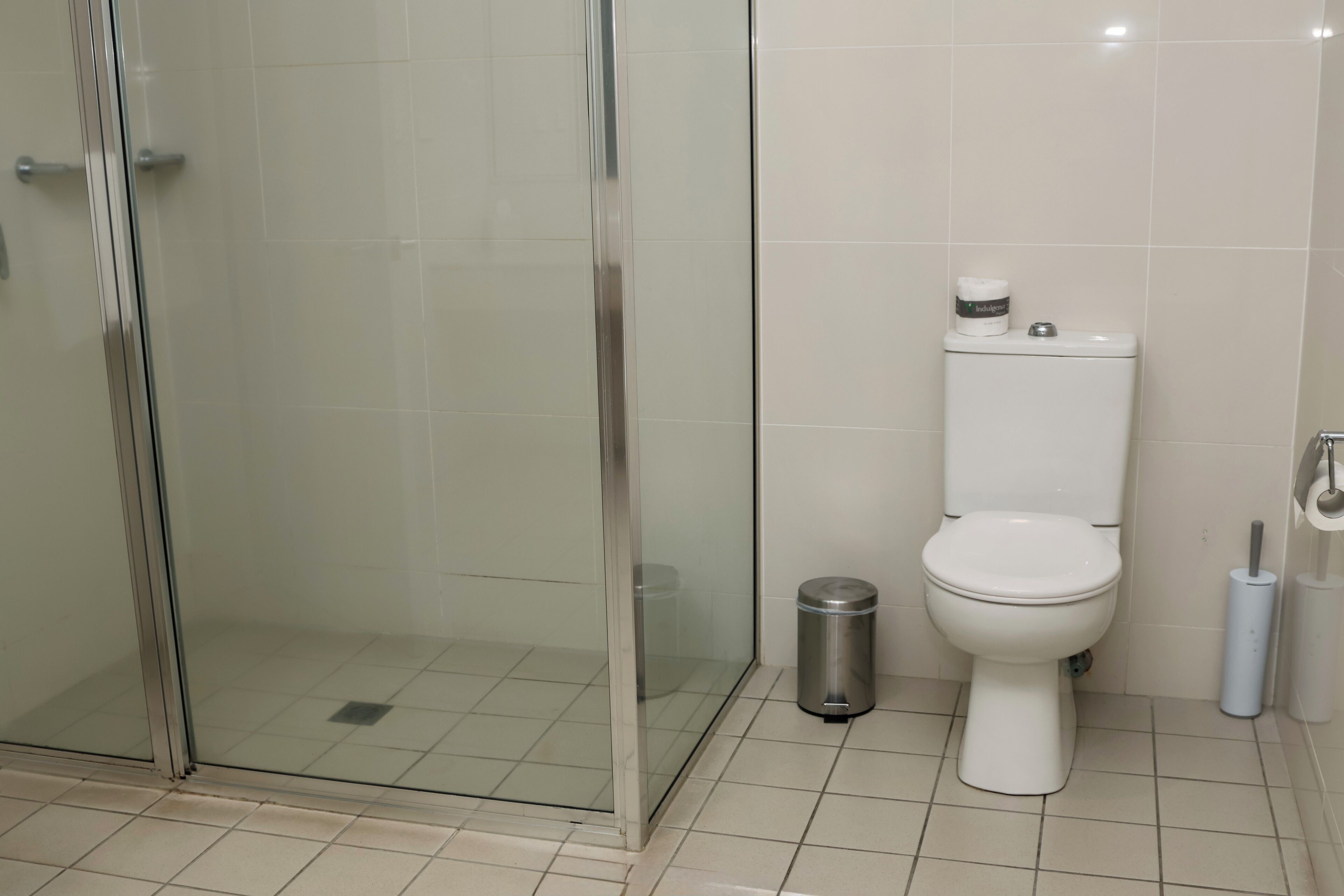 Un baño con ducha de vidrio, inodoro y un cubo de basura.