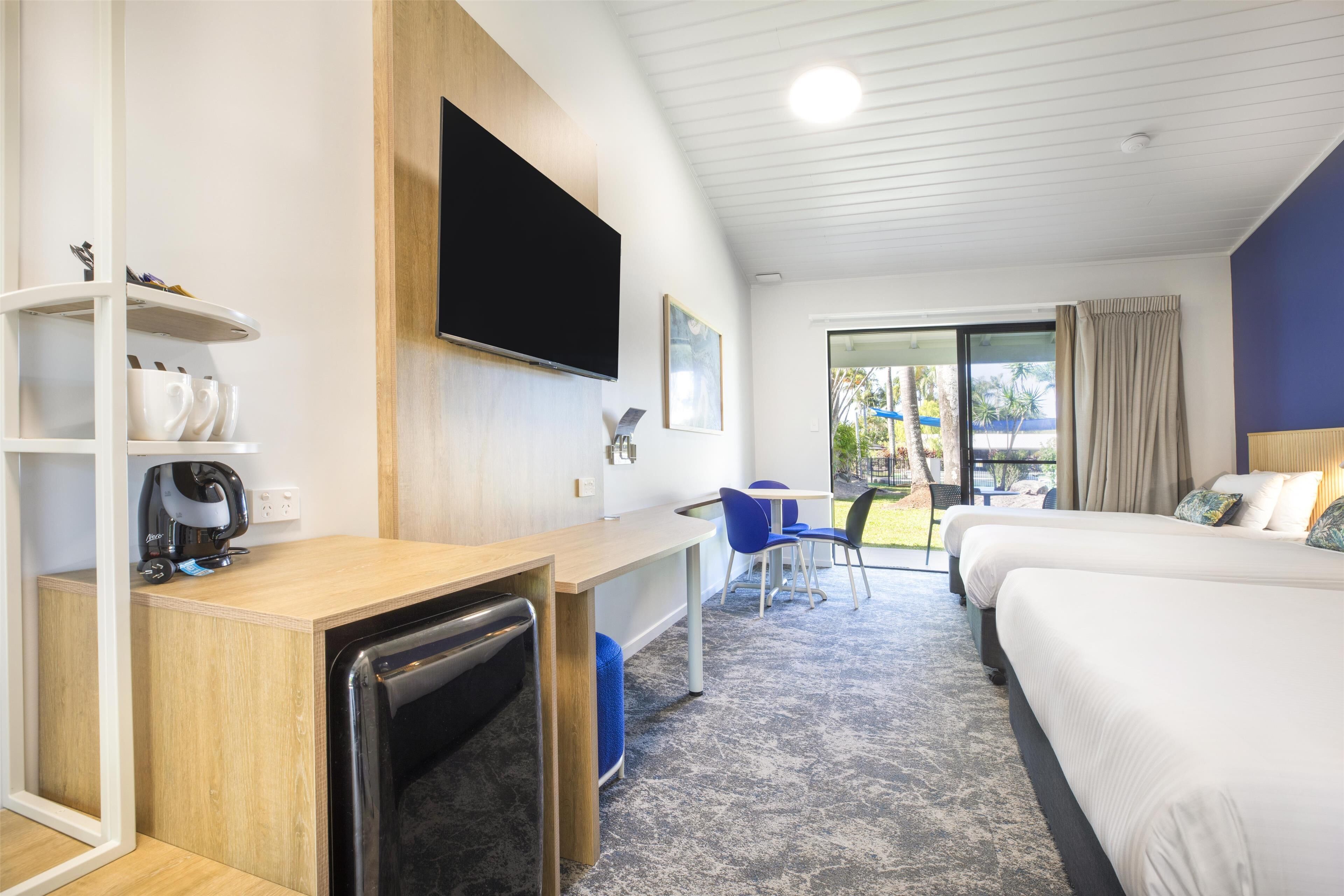 Ein Hotelzimmer mit Bett, Schreibtisch, Fernseher, Kaffeemaschine und Blick ins Freie.
