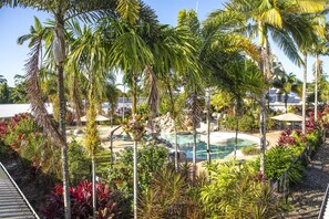 Una piscina rodeada de palmeras y plantas tropicales, con sillas de descanso y sombrillas al fondo.