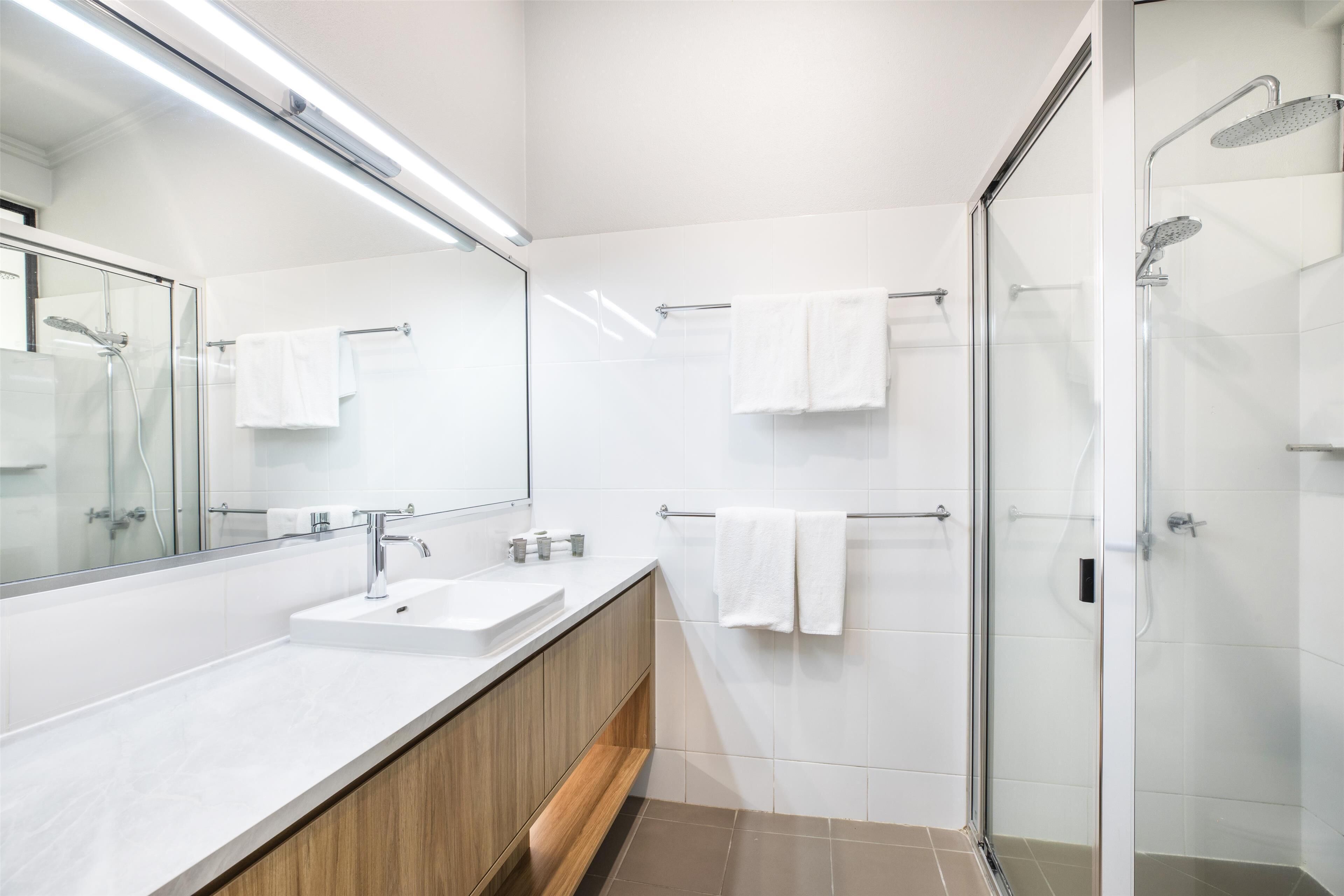 A modern bathroom with a glass shower enclosure, a large mirror, and a wooden vanity.