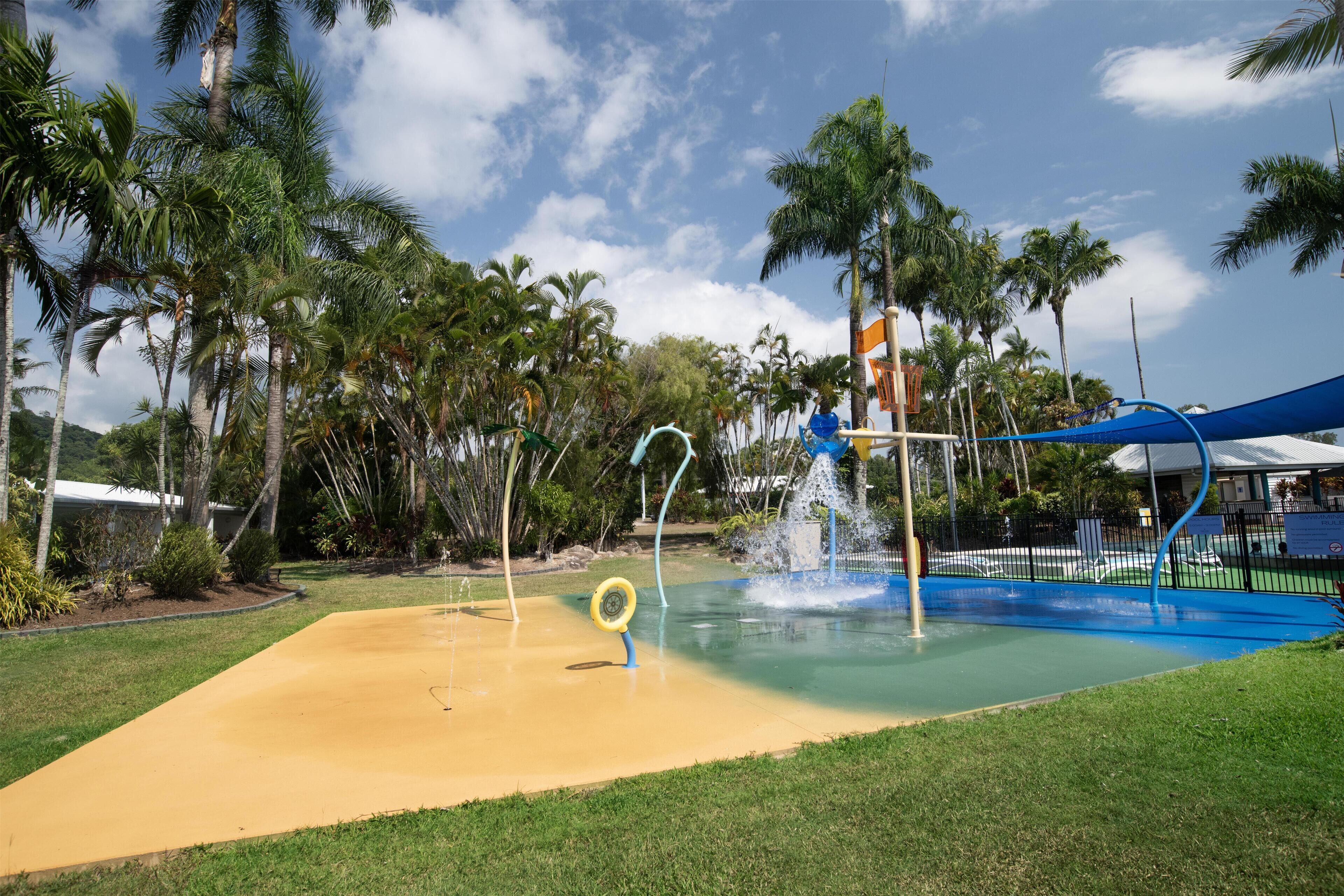 Een waterpark met een spuitzone, palmbomen en een blauw dak.