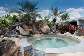 Un jacuzzi rodeado de rocas y palmeras, con una cascada.