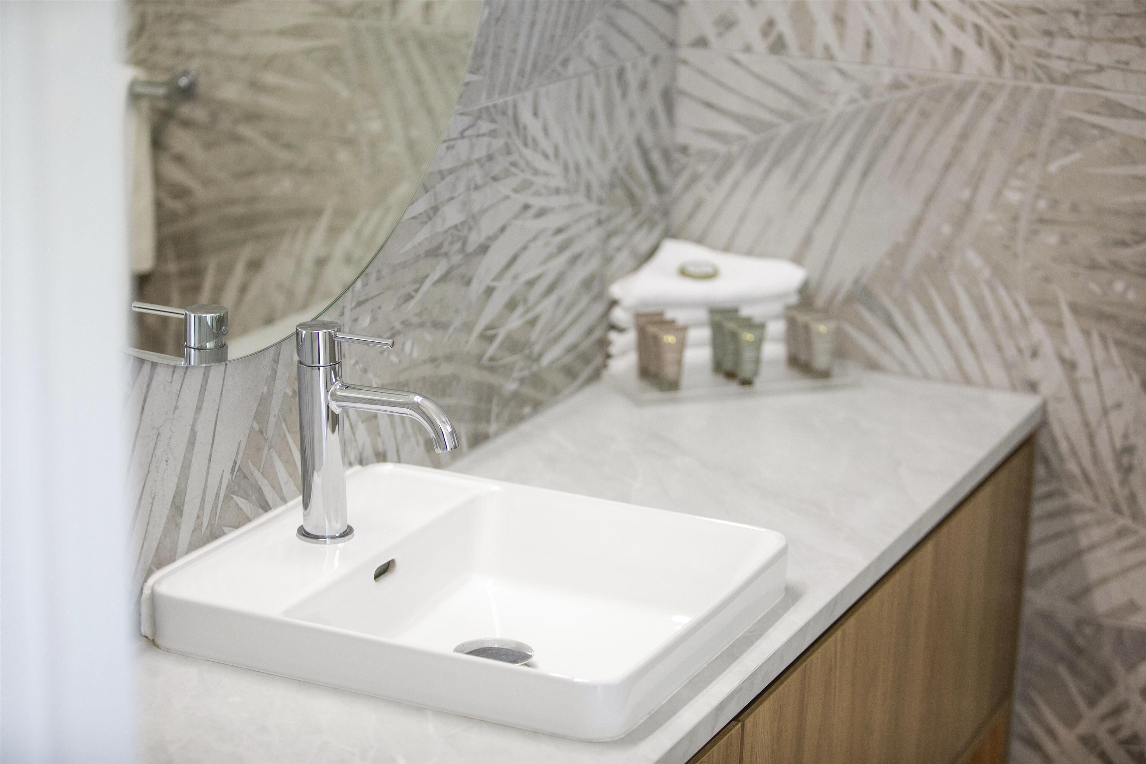 Un baño con lavamanos blanco, grifo cromado y mueble de madera.