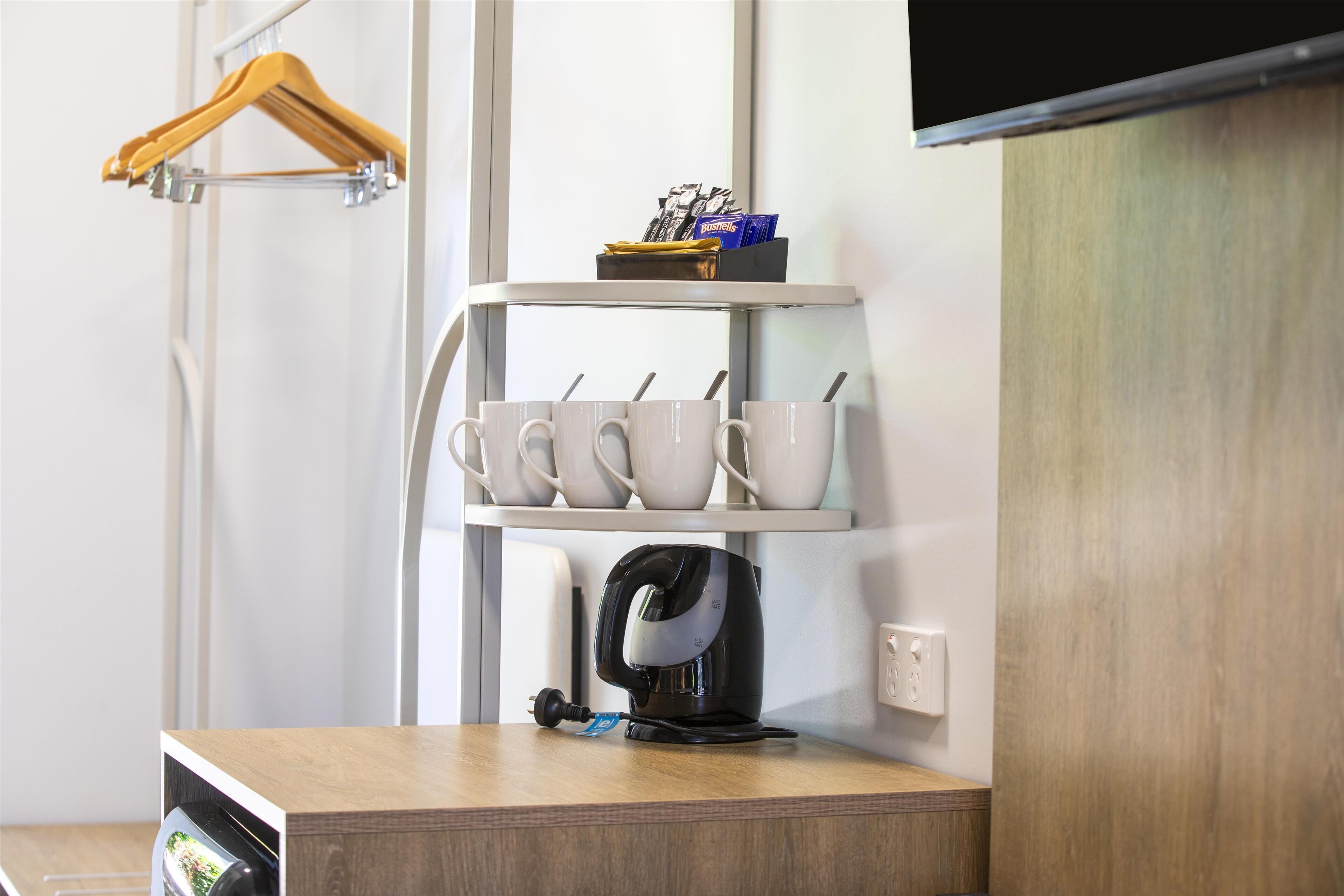 A kitchenette with a coffee maker, mugs, and a shelf with utensils.