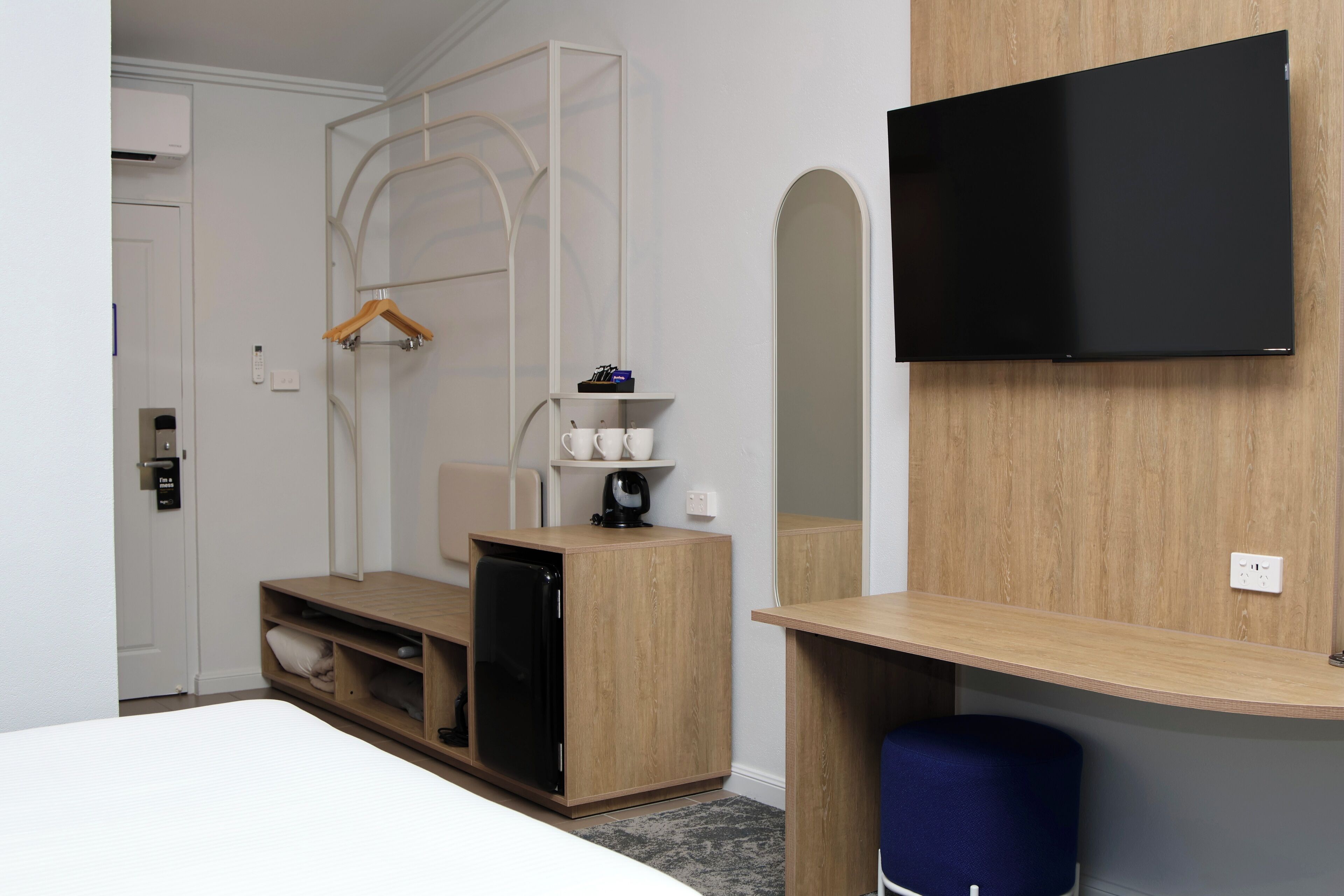 A modern hotel room with a bed, a desk with a computer, a TV, and a wardrobe.