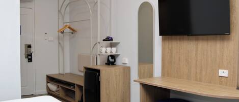 A modern hotel room with a bed, a desk with a computer, a TV, and a wardrobe.