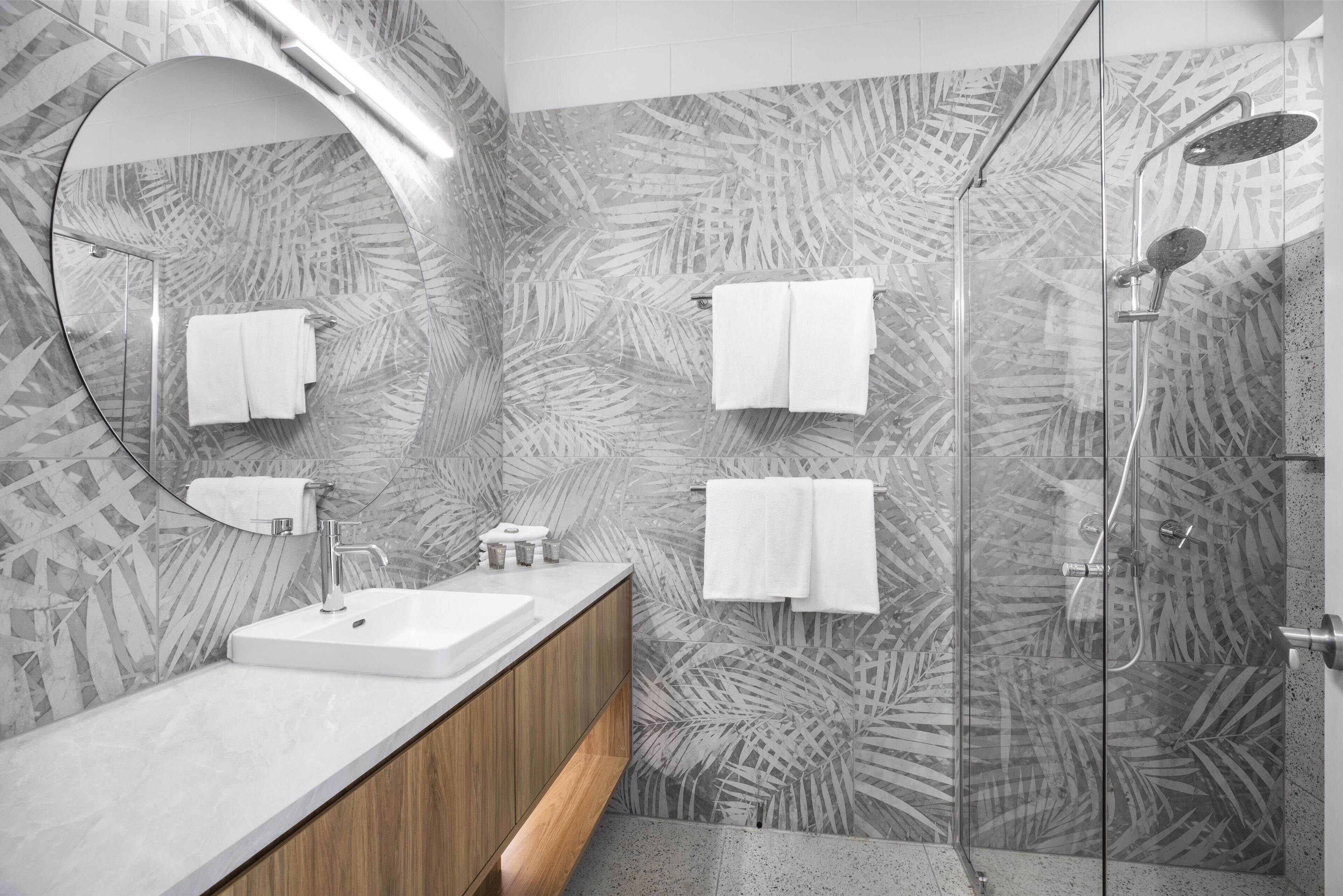 Un baño moderno con lavamanos de mármol, tocador de madera y mampara de ducha con un mosaico de hojas.