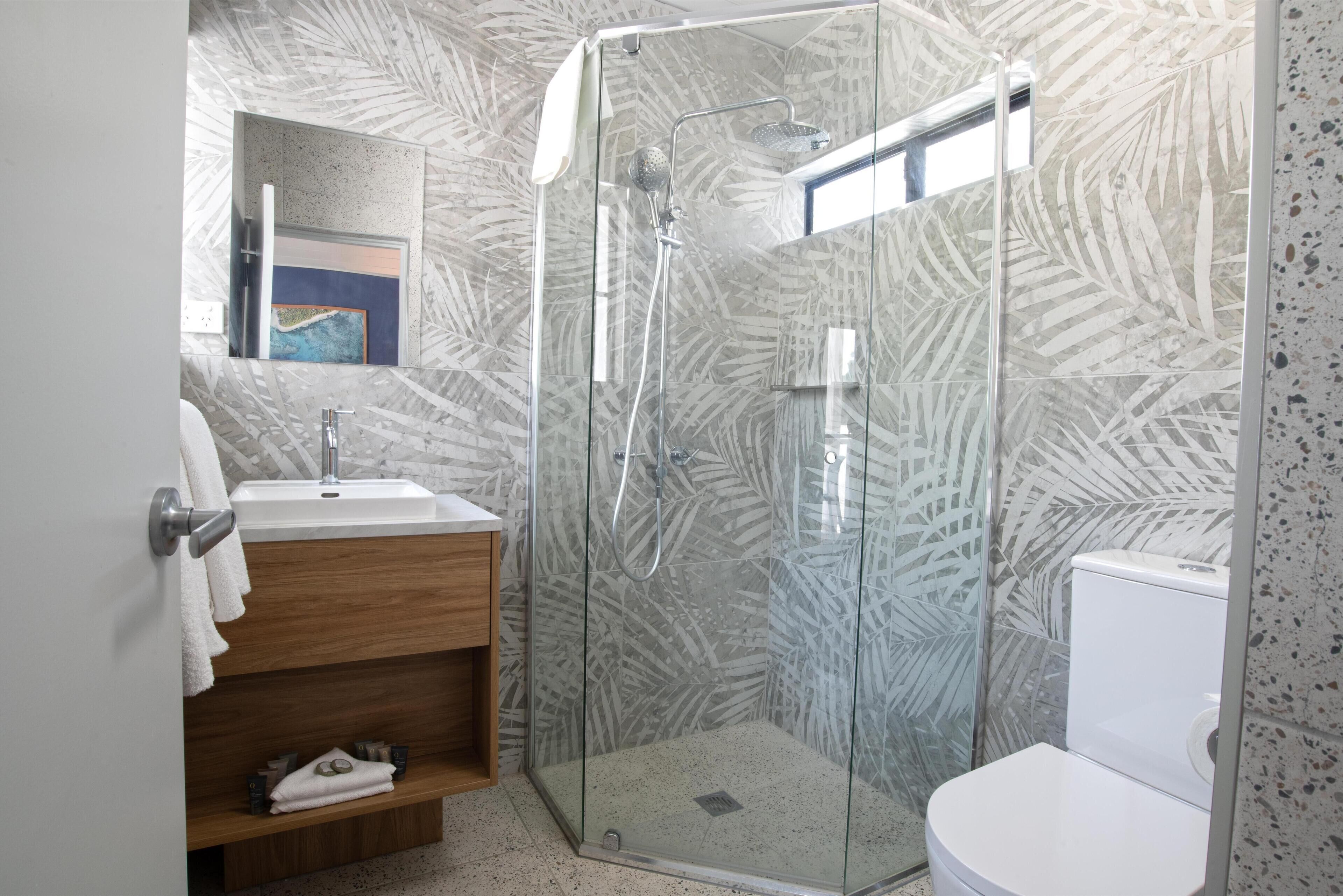 Un baño moderno con ducha de vidrio, lavamanos blanco y retrete.
