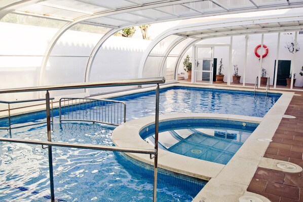 An indoor swimming pool with a curved design, surrounded by a glass enclosure, and equipped with a lifebuoy on the wall.