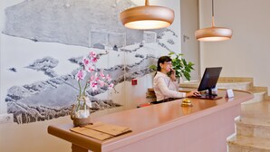 A reception desk with a modern design, a digital screen, and a vase with pink flowers. - Hotel Jeni & Restaurant (Mercadal)