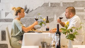 A dining table with wine glasses, a bottle of wine, and a vase with flowers. - Hotel Jeni & Restaurant (Mercadal)