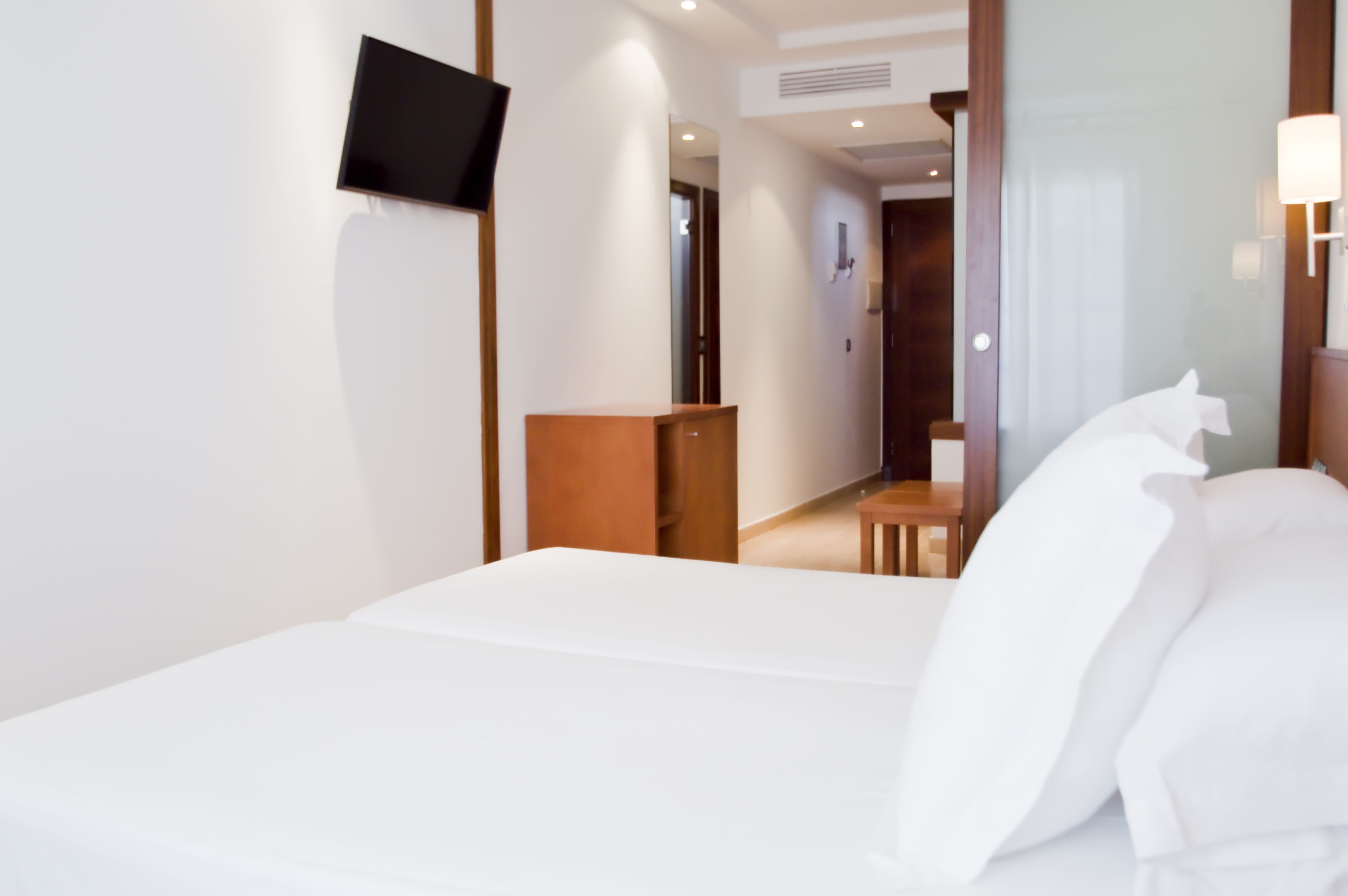 A hotel room with a bed, a TV mounted on the wall, a wooden nightstand, and a small table.