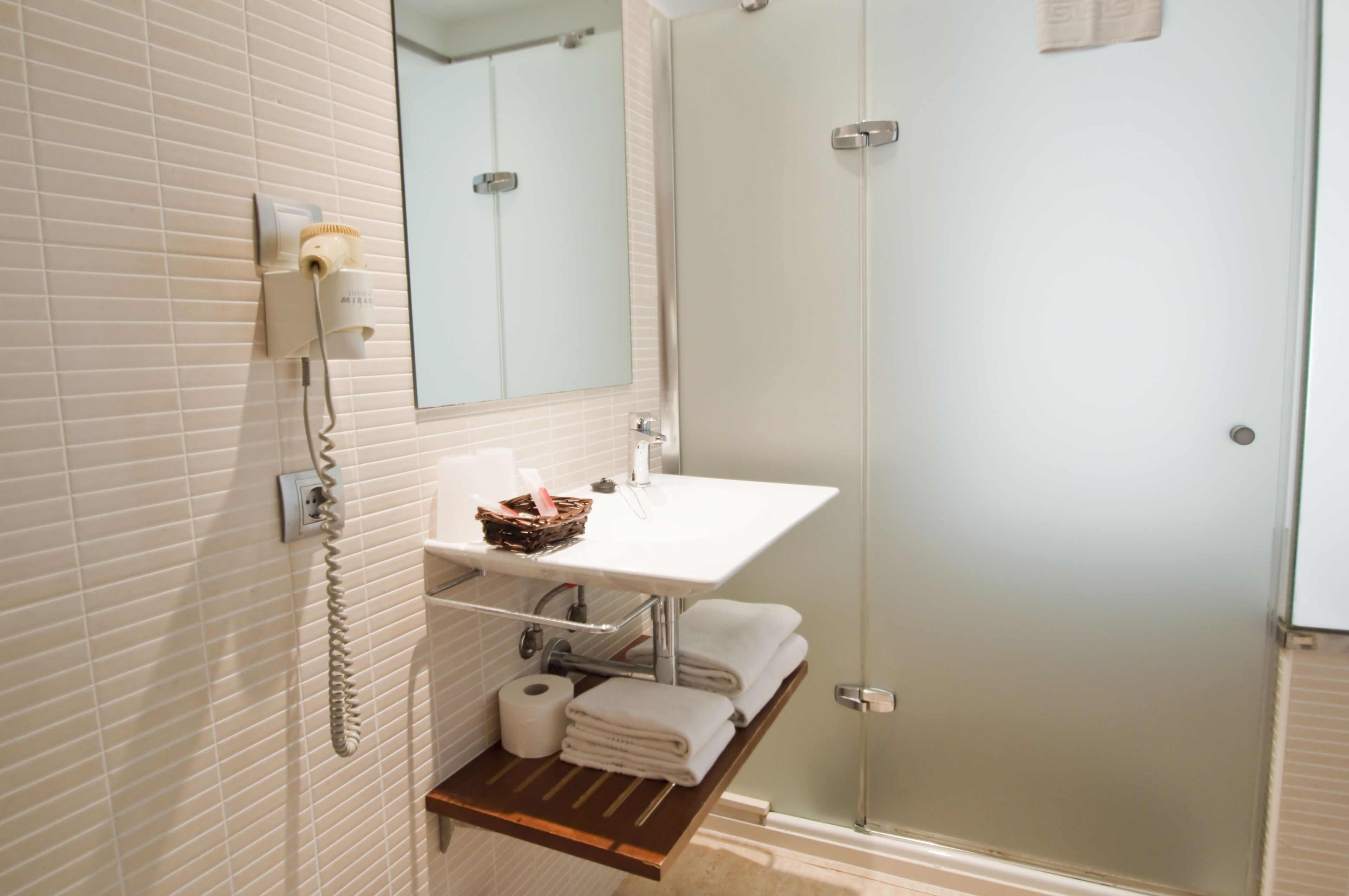 A bathroom with a white sink, a mirror, a towel rack, a shower, and a telephone.