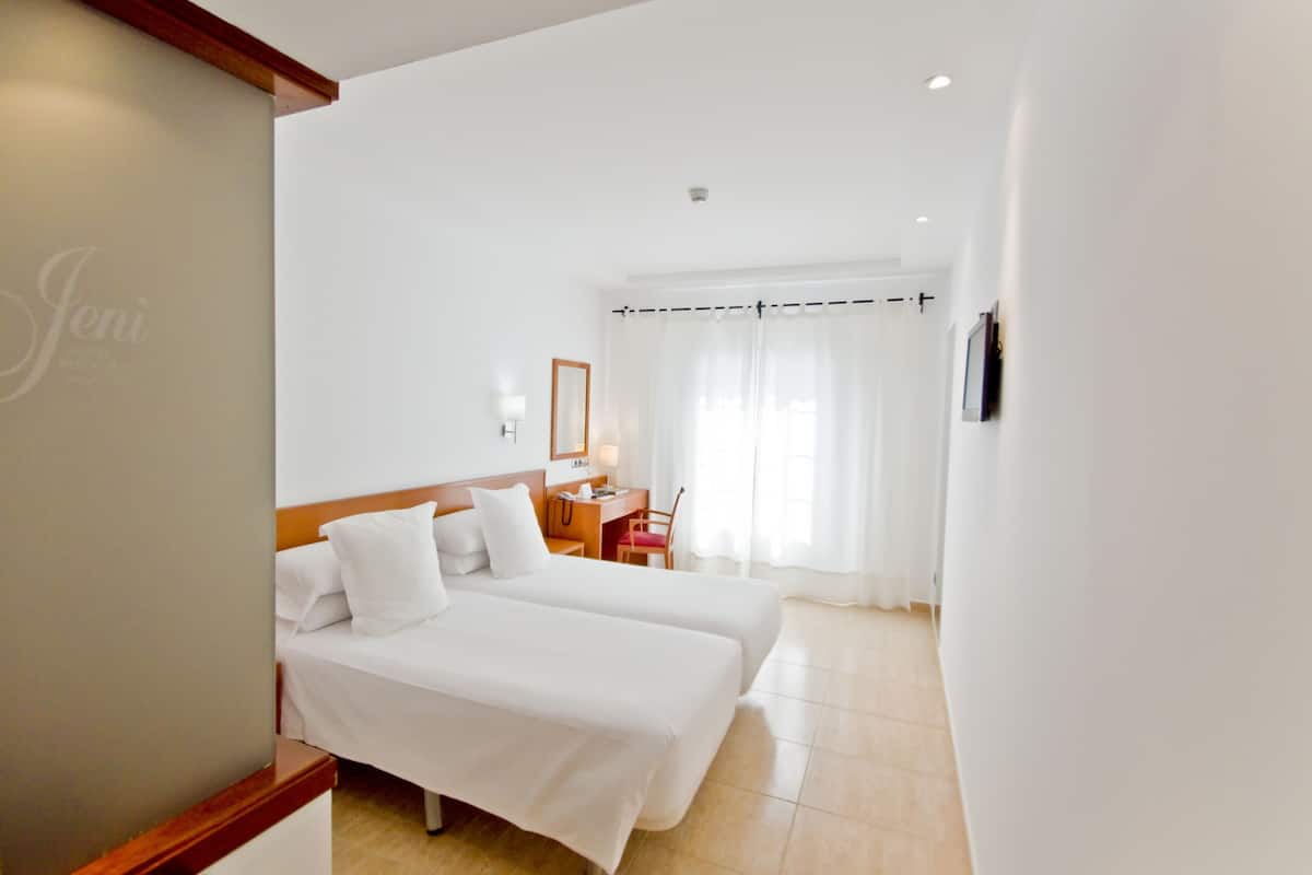 A hotel room with two beds, a desk, a chair, and a window with curtains.