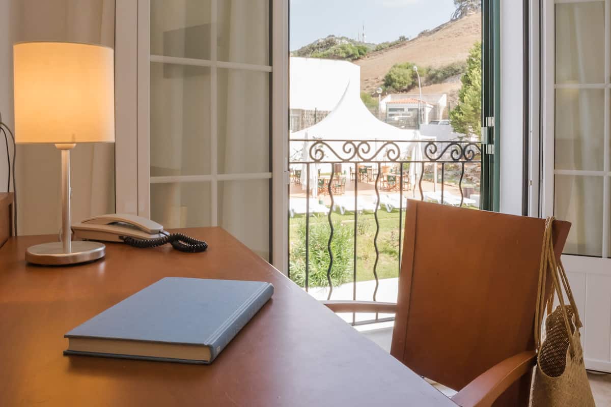 A room with a wooden desk, a lamp, a telephone, and a chair.