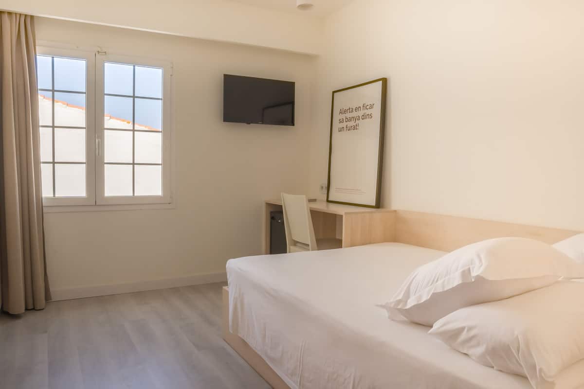 A hotel room with a bed, a desk, a chair, a TV, and a window with curtains.