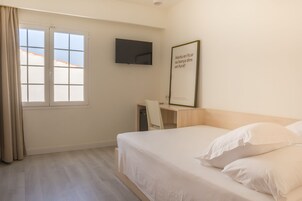 Una camera d'albergo con un letto, una scrivania, una sedia, una televisione e una finestra con tende.