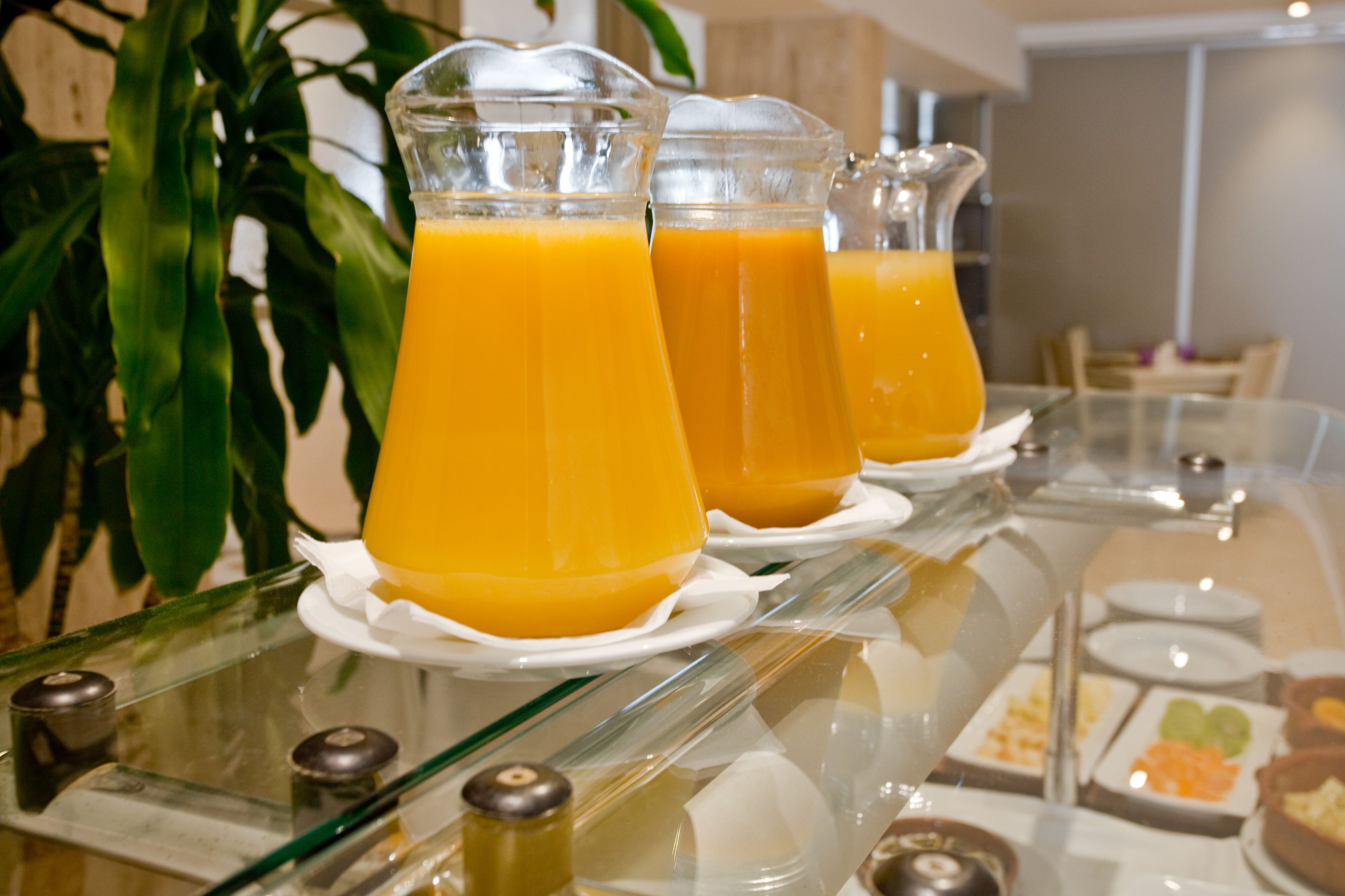 A buffet table with clear glass pitchers of orange juice, white plates, and various food items.