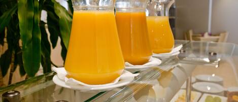 A buffet table with clear glass pitchers of orange juice, white plates, and various food items.