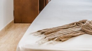 A hotel room with a bed, a wooden desk with a lamp, a chair, and a view of the outside through a window. - Hotel Jeni & Restaurant (Mercadal)