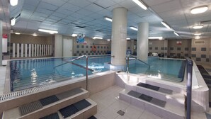 Una piscina techada con múltiples carriles, escalones para entrar y un techo azulejado con iluminación fluorescente.