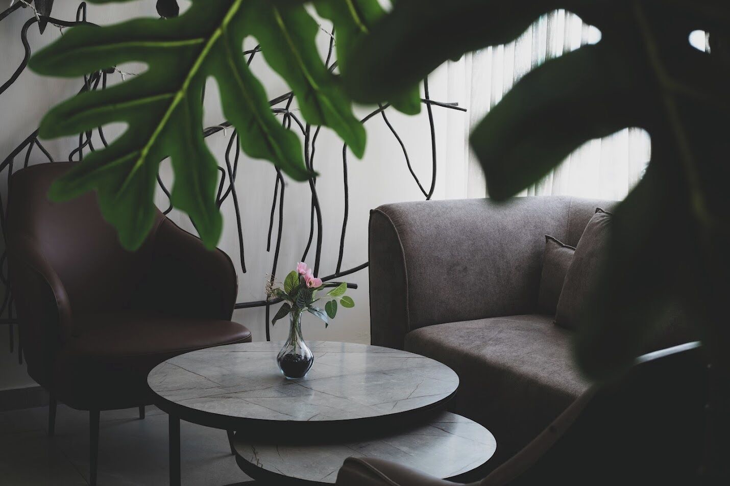 Un salon moderne avec une table ronde en marbre, un canapé en cuir marron foncé et un vase rempli de fleurs roses.