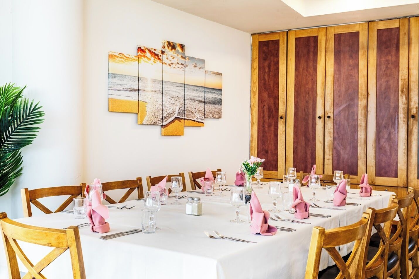 Un comedor con una mesa blanca dispuesta para varios comensales, sillas de madera y un aparador grande al fondo.