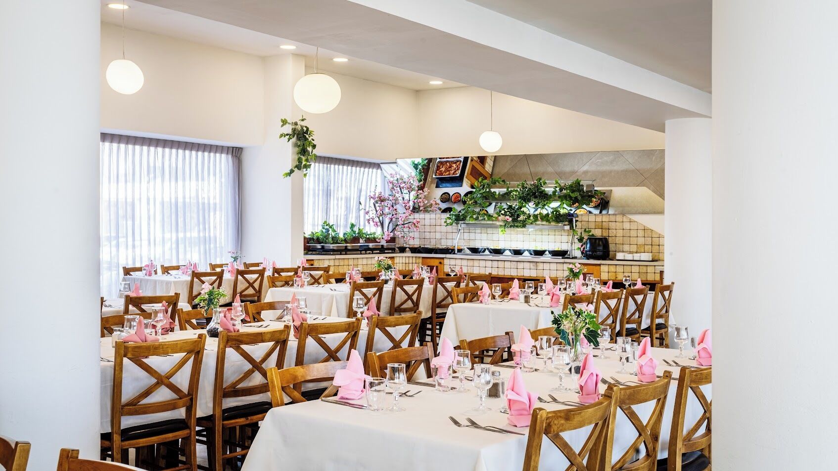 Un restaurante con varias mesas listas para comer, sillas de madera y una zona de cocina al fondo.