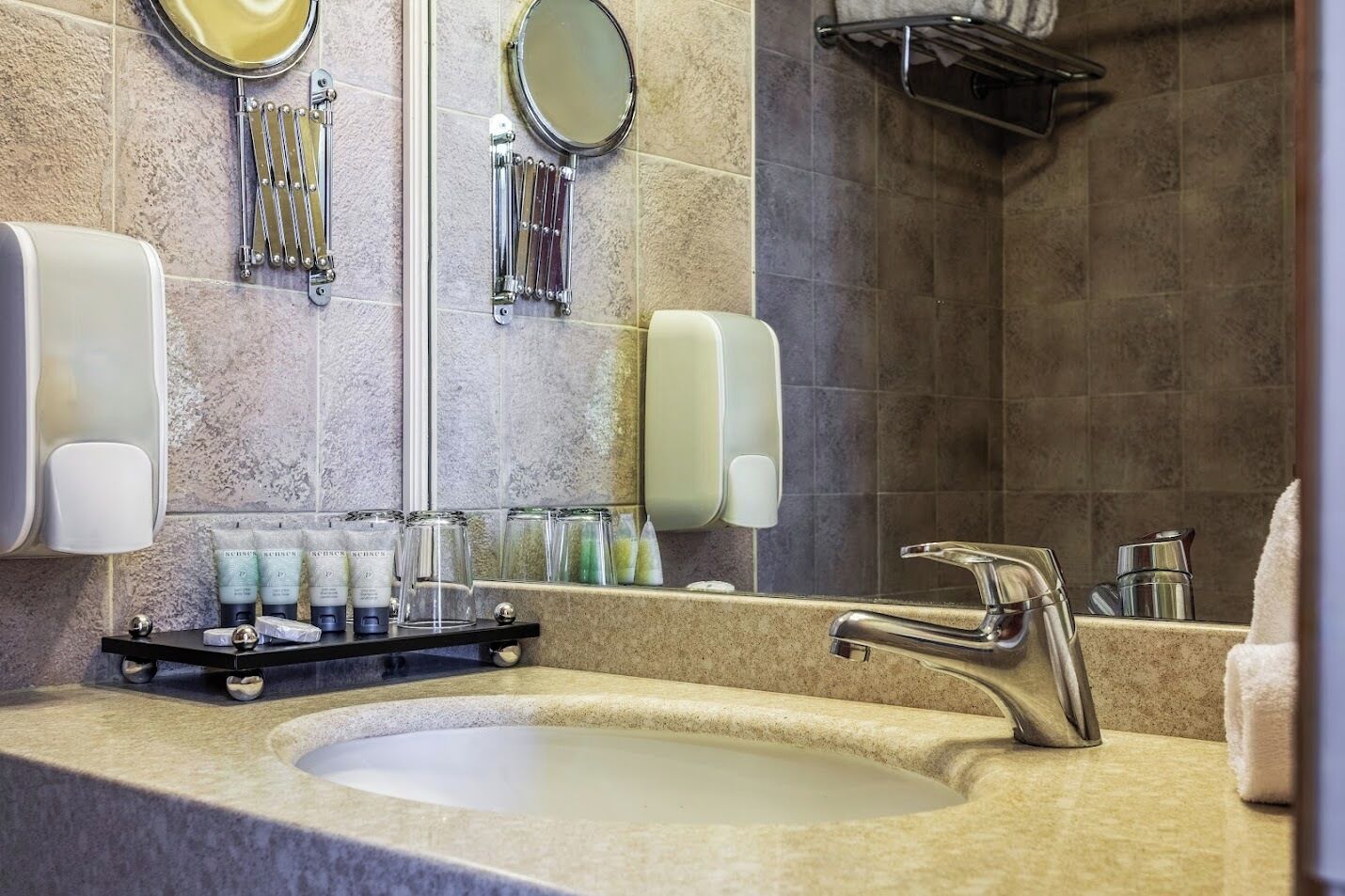 Un baño moderno con un lavamanos grande, dos dispensadores de jabón para manos, un espejo y un perchero para toallas.