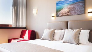 Una habitación de hotel con una cama grande, un sillón rojo y un cuadro de una playa.