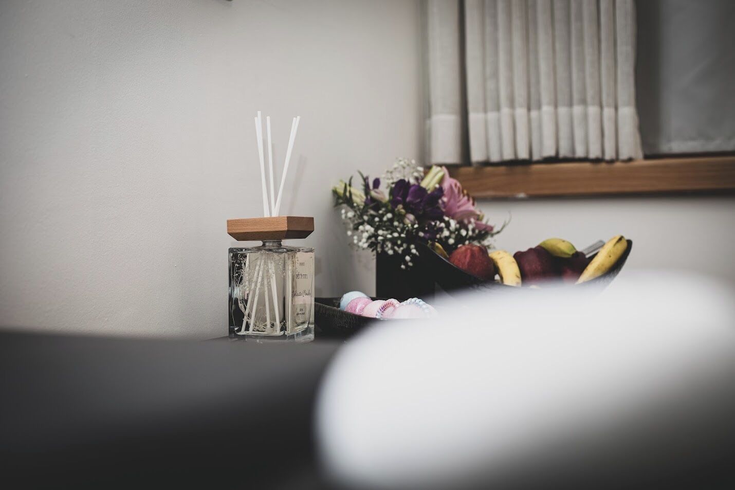 A room with a small table holding a glass container with reed diffusers and a bouquet of flowers.