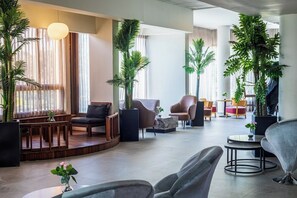 A spacious lobby with a wooden bench seating area, multiple chairs, and potted plants. - Inbar Hotel (Arad)